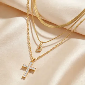 Gros plan d'un collier en or à trois rangs avec chaîne serpent, lettre D et croix.