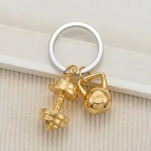 Detail view of sports style gold dumbbell and kettlebell metal keychain pendant for gym fans.