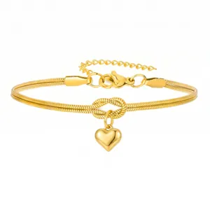 Close-up van de gouden slangenketting armband met hartvormige hanger en een sierlijke knoop.