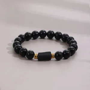 Close-up detail of natural black obsidian beaded bracelet with gold spacer and central stone.