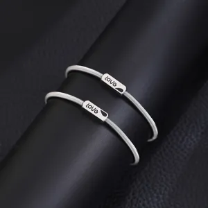 Stainless steel spring couple bracelets detail view with engraved love tag on black display.
