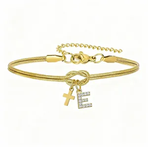 Dettaglio del bracciale a catena serpente dorata con nodo, croce e ciondolo con lettera E.