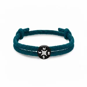 Dunkelgrünes geflochtenes Seilarmband mit schwarzem Kompass-Anhänger, minimalistischer Reiseschmuck.