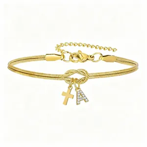 Primo piano del bracciale catena serpente dorata con nodo d'amore, croce e ciondolo con lettera.
