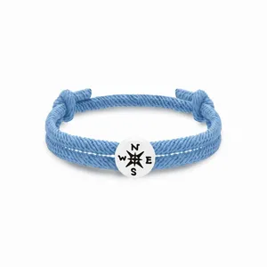 Nahaufnahme des blauen geflochtenen Seilarmbands mit einem runden Kompass-Metallanhänger.