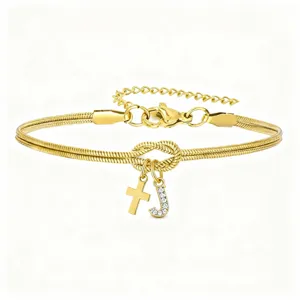 Primo piano dei dettagli del bracciale serpente doro con ciondolo a croce e lettera J strass.