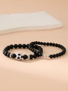 Dettaglio di bracciali di perline nere opache da uomo con calcio e ciondolo con lettera S dorata