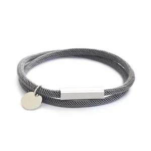 Vista dettagliata del bracciale in corda grigia con chiusura magnetica e targhetta rotonda.