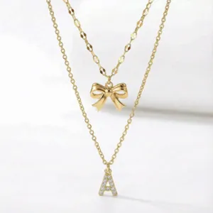 Primo piano della collana dorata a doppio strato con fiocco e ciondolo a lettera brillante.