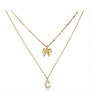 Elegante collana dorata a doppio strato con grazioso fiocco e ciondolo lettera C in strass brillanti.