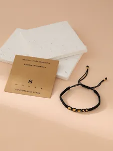 Close-up of the black braided Morse code number bracelet with golden beads and card detail.