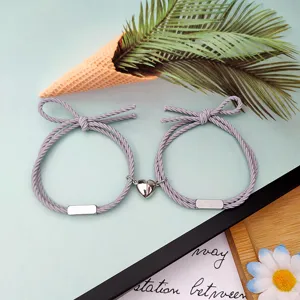 Nahaufnahme von Partner-Armbändern mit magnetischem Herzanhänger und grauem geflochtenen Seil.