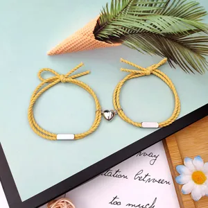 Paar magnetische geflochtene Seilarmbänder mit Herzanhänger, stilvoller gelber Kordschmuck Detail.