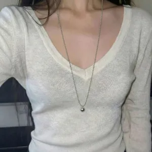 Nahaufnahme einer minimalistischen langen silbernen Perlenkette mit rundem Anhänger.