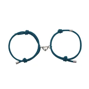 Close-up van bijpassende teal gevlochten koppelarmbanden met magnetische hartbedels.