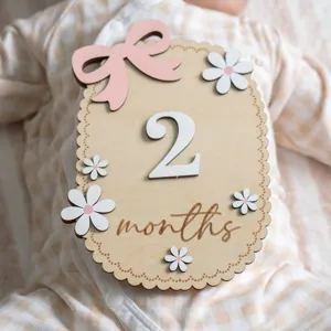 Detail view of a wooden baby milestone card featuring 2 months text and floral decor