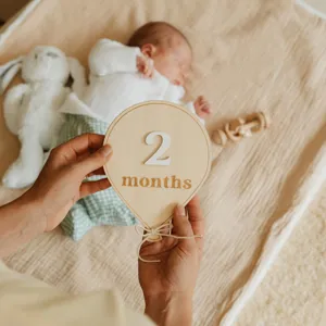 Wood baby monthly milestone card detail showing 2 months design in cozy newborn photography scene.