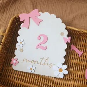Close-up detail of a wooden baby milestone month card with pink bow and flower decor in basket.