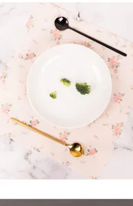 Detailed close-up shot of pink floral placemat with white plate and spoons on marble surface.