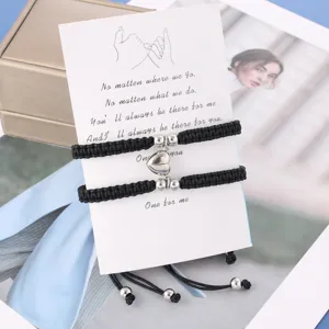 Primo piano dei bracciali di coppia intrecciati neri con cuore magnetico su cartoncino.