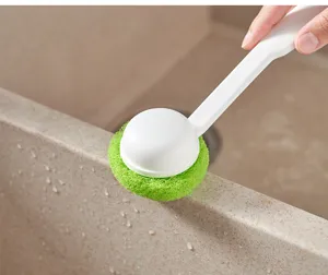 Close-up detail of the long-handled cleaning brush with green sponge ball working on sink.