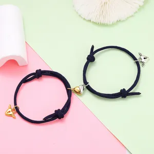 Detail view of matching couple magnetic heart braided bracelets with cute winged lock charms.
