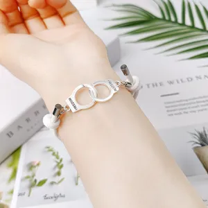Gros plan du bracelet menotte argenté sur corde blanche, détail de bijoux de couple élégants.