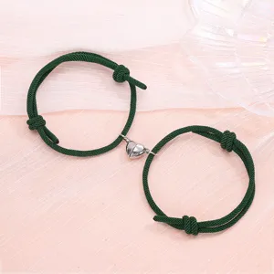 Detail view of magnetic couple bracelets featuring dark green braided cords and half heart alloy charms.