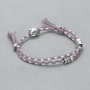 Closeup of braided cord bracelet featuring alloy buddha head and carved barrel beads details.