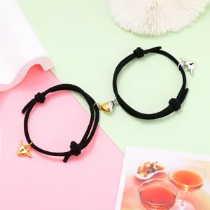 Close-up detail of black rope couple bracelets with magnetic heart charms and cute wing locks.