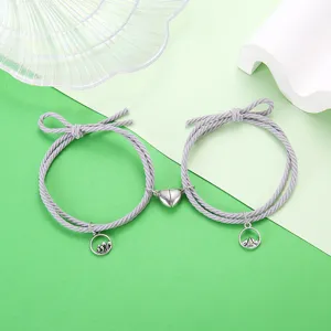 Minimalistische koppelarmbanden van gevlochten touw met berg- en golfhangers detail.