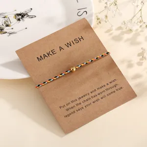 Detail view of a handmade colorful braided string bracelet with a golden bead on wishing card.