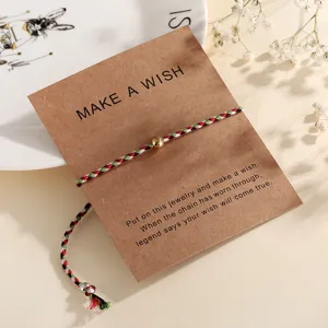 Handcrafted braided wish bracelet with golden bead and kraft paper card display detail close up.