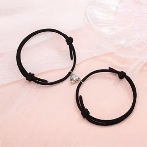 Detailed view of black braided couple bracelets featuring a magnetic metal heart clasp design.