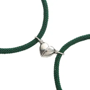 Detailopname van magnetische hartje koppelarmbanden met groen gevlochten touw en metalen bedel.