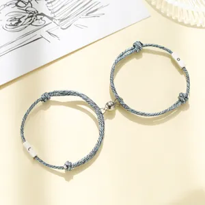 Detail view of magnetic couple bracelets featuring sun and moon charms on blue woven rope.