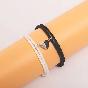 Close-up detail of black and white woven couple bracelets with magnetic heart charm design.