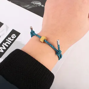 Paracord survival bracelet detail featuring blue black woven cord and gold gear bead charm.