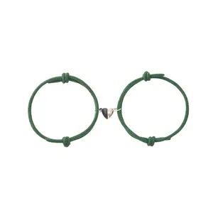 Green woven cord couple bracelets with magnetic black and white heart charm detail.