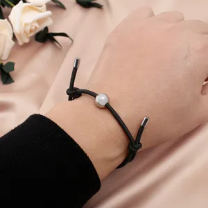 Detail view of the black cord bracelet with a metallic silver bead and adjustable ends.