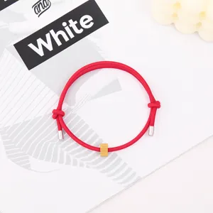 Close-up detail of a vibrant red braided rope bracelet featuring a golden cylindrical bead.