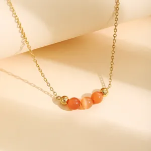Gros plan sur un élégant collier chaîne doré brillant orné de perles œil de chat orange.