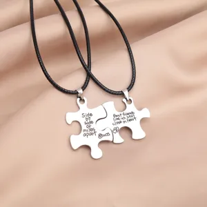 Close-up detail view of matching puzzle piece pendant necklaces with engraved emotional text.