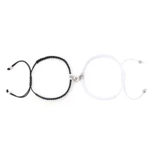 Primo piano di bracciali da coppia intrecciati in bianco e nero con ciondolo a cuore magnetico.