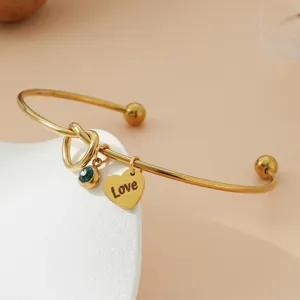 Gros plan détaillé sur un bracelet jonc doré en acier inoxydable avec pendentif cœur.