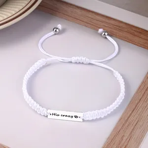 Detailed shot of white braided rope couple bracelet with engraved metal bar and heart symbol.
