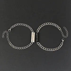 Close-up detail of stainless steel couple matching chain bracelets with engraved tags.