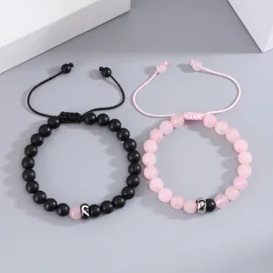 Dettaglio di bracciali di coppia in perline nere opache e rosa con ciondoli a cuore divisi.