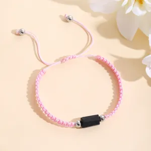 Primo piano dettagliato del bracciale intrecciato rosa fatto a mano con pietra nera.