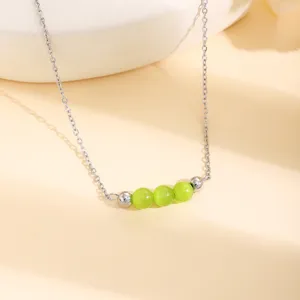 Gros plan de détail d'un collier chaîne argenté avec perles œil-de-chat vertes et intercalaires.
